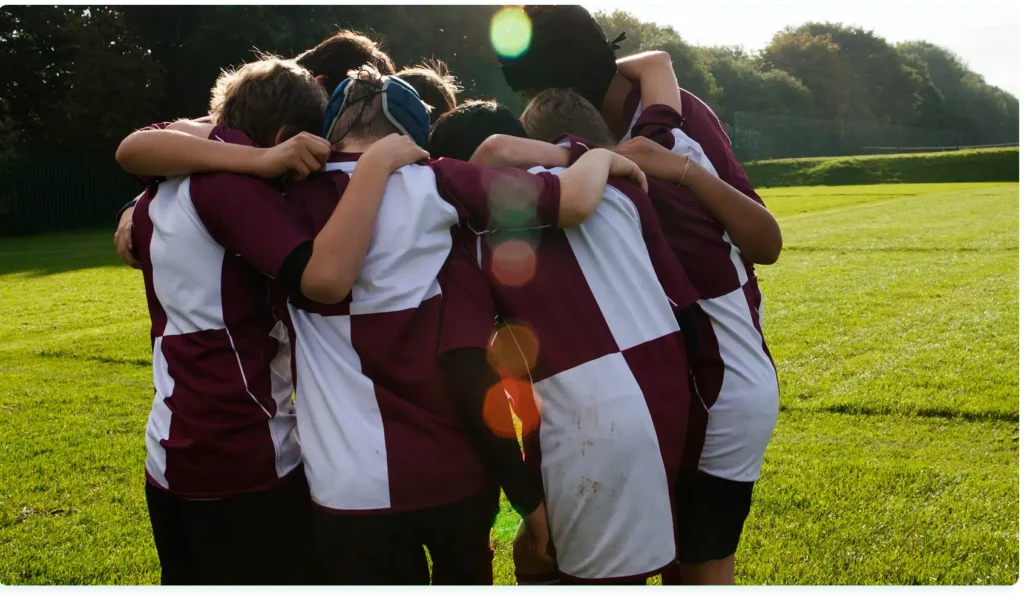 Een groep jonge rugbyspelers vormt een kring op het grasveld en omhelst elkaar om hun eenheid en teamgeest tijdens de wedstrijd te tonen.